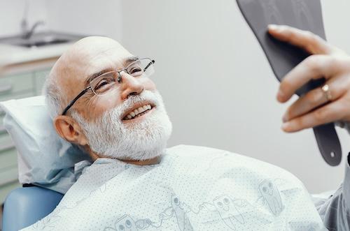 Older man holding mirror looking at his teeth, scottsdale az